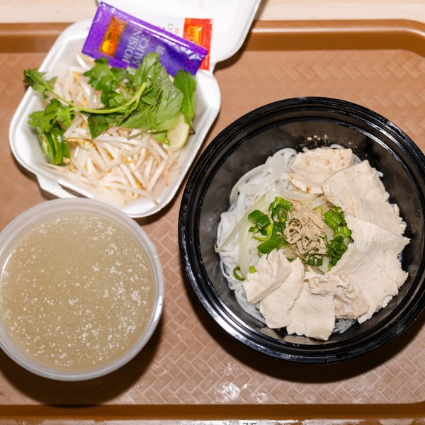 A pho takeout meal with chicken, noodles, broth, and a side of fresh herbs and bean sprouts.