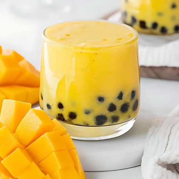 A glass of mango boba tea with diced mango pieces on a white surface.
