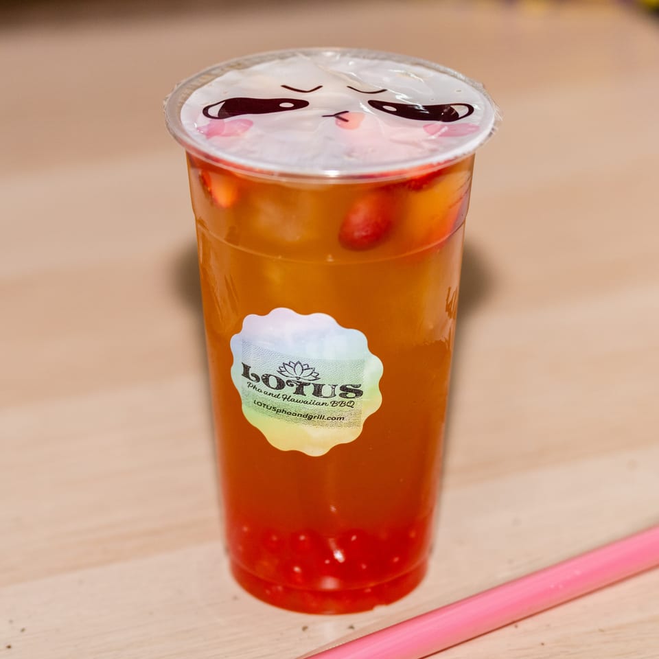 A Lotus Pho and Hawaiian BBQ fruit tea with strawberries and popping boba, and a pink straw.