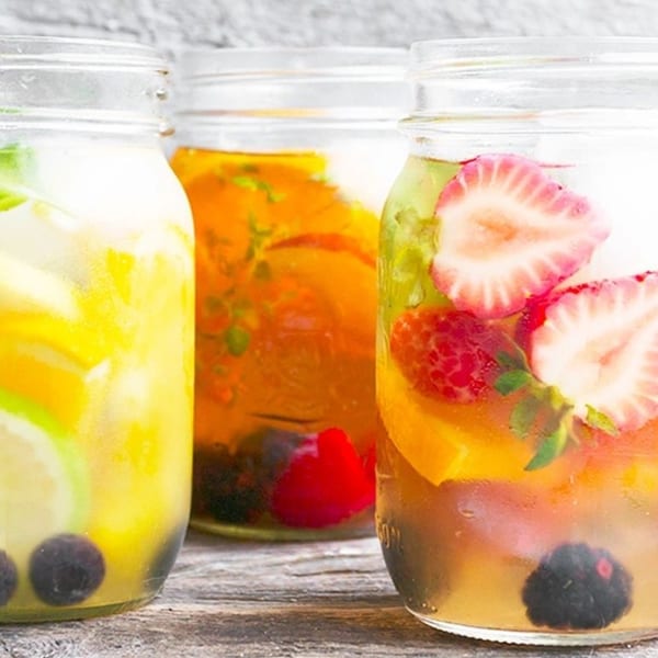 Three mason jars filled with colorful fruit-infused drinks, including strawberries, blueberries, and citrus.
