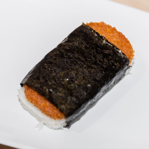 A close-up of a Spam musubi, featuring crispy orange Spam, white rice, and dark nori.