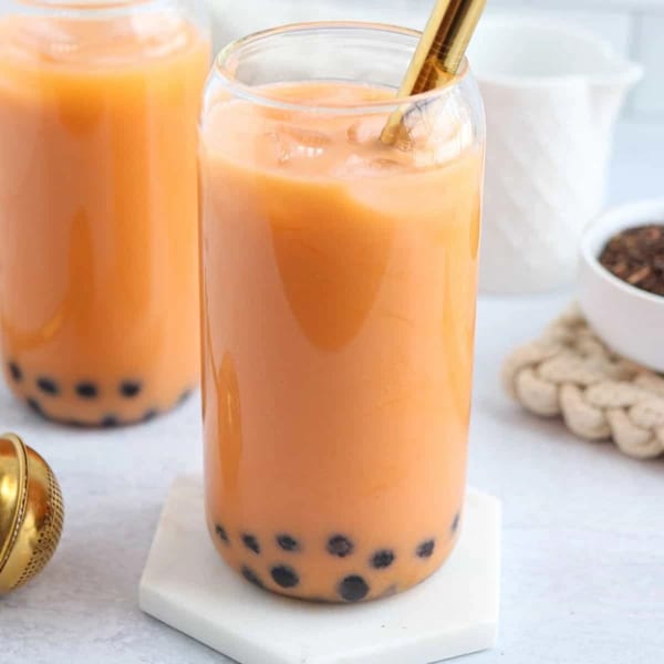 Two glasses of orange Thai iced tea with boba pearls and a gold straw.