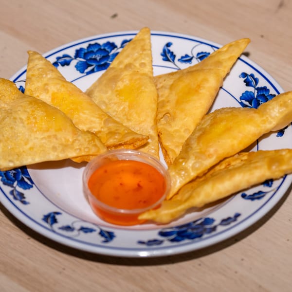 Golden fried wontons with a side of sweet chili dipping sauce on a blue and white plate.