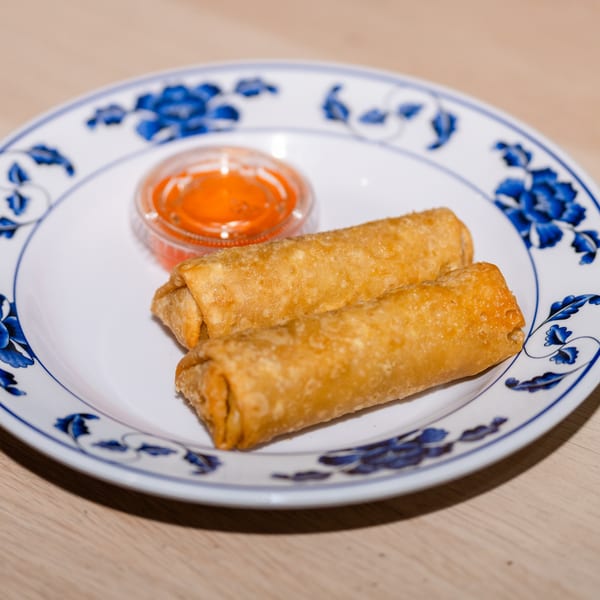 Two crispy golden egg rolls with a side of orange dipping sauce on a white and blue plate.